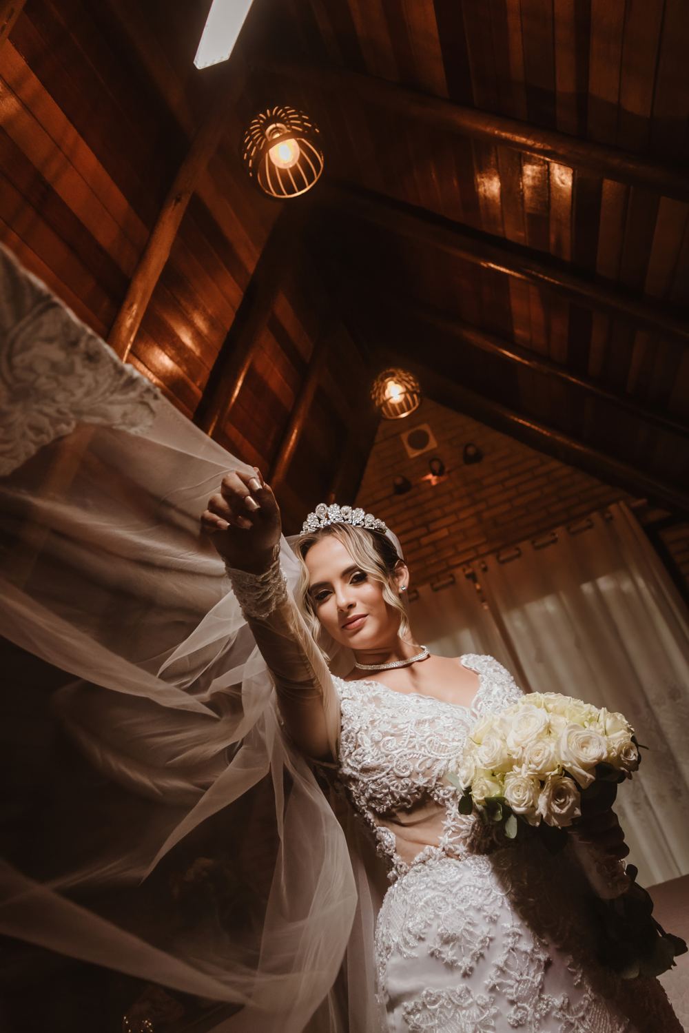 Noiva com o véu ao vento, segurando um buquê de rosas brancas